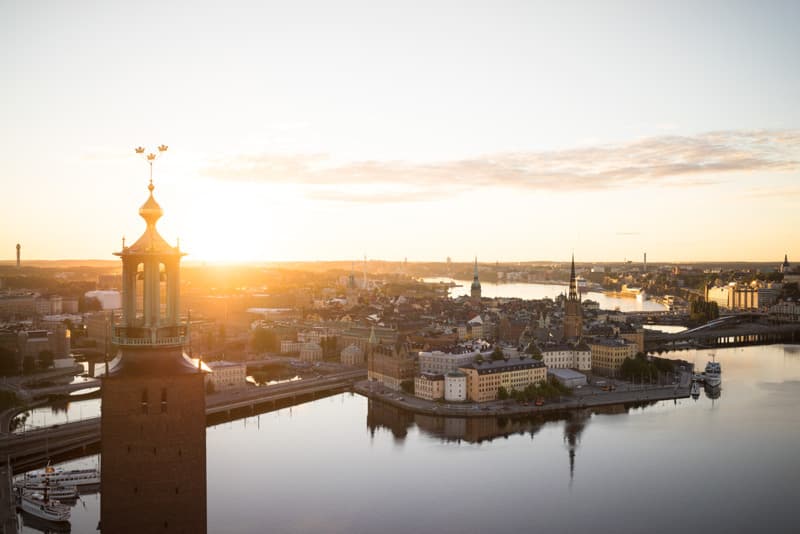 Sunrise over City Hall and the Old Town Aerial view of Stockholm City Hall tower backlit by the sun, with the Old Town and surrounding water glowing in soft morning light.