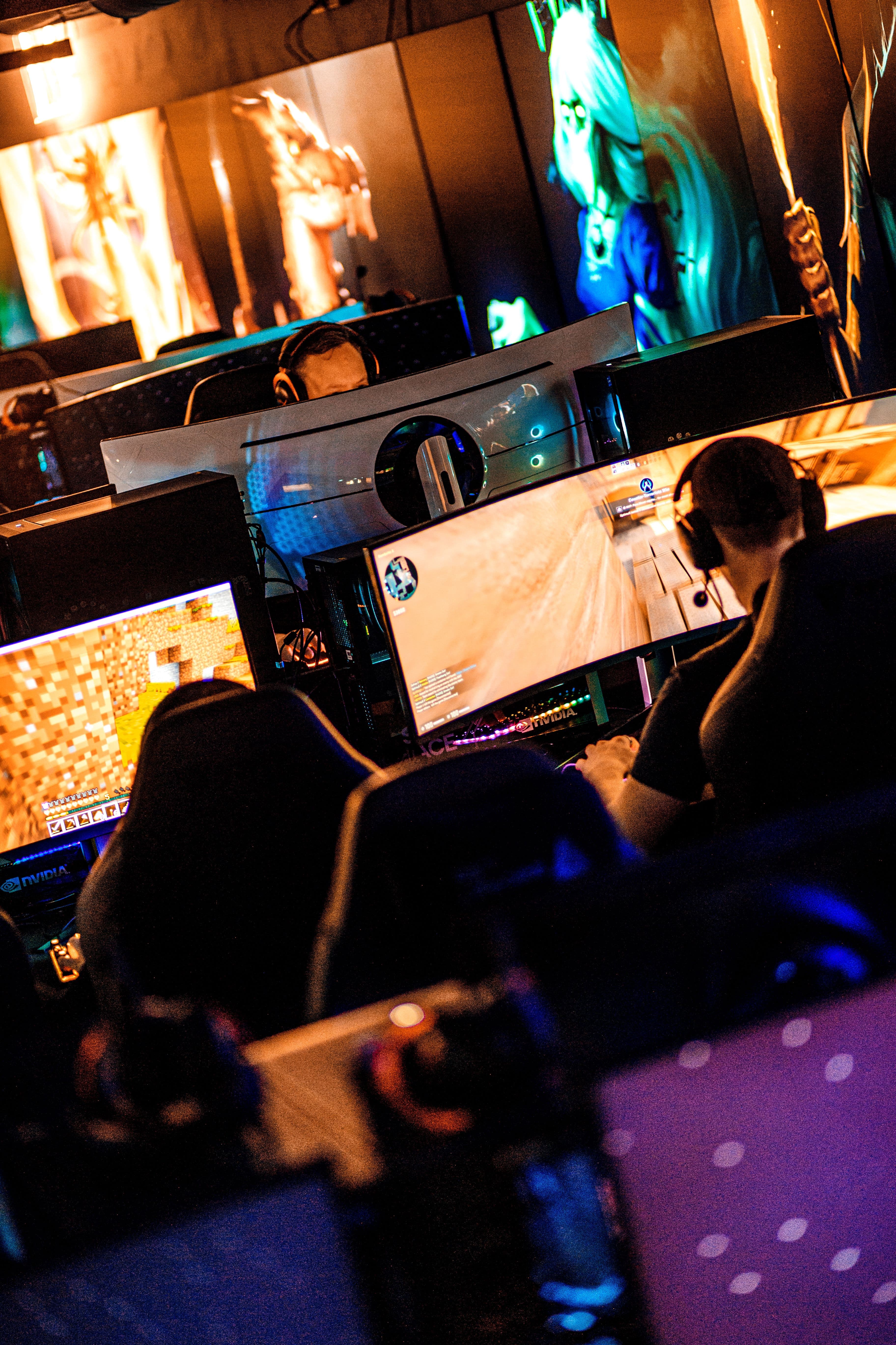 Flera gamers sitter med headset framför stora skärmar i ett färgglatt e-sportrum.